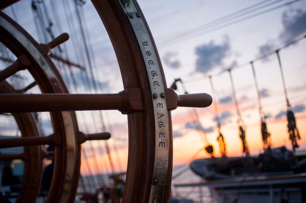 Ship helm made out of wood with sunsetting on the background.